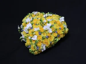Rouw bloemstuk Protea. Een bloemstuk in de vorm van een hart, met gele, witte en paarse bloemen. Gemaakt door Bloeibloemen.nl