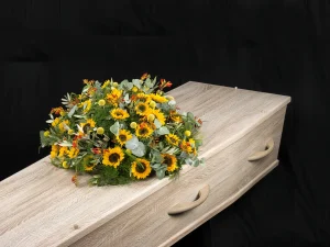 Rouw bloemstuk Sun of Love. Een rond bloemstuk met zonnebloemen en andere gele en rode bloemen erin op een kist.