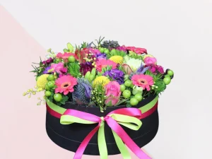 Flower box Color Big, een box met verschillende soorten bloemen in de kleuren geel, roze, paars, rood en groen, gestoken in een blok oase. Deze bloemen zitten in een zwarte box met roze en groen lint eromheen.