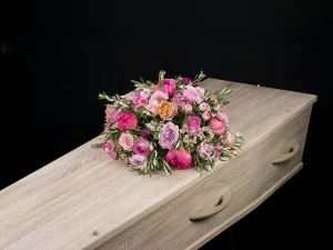 Pink of Goodbye, een rouw bloemstuk in de kleuren roze en paars in een ronde vorm, deze ligt op een kist. Het boeket is gemaakt door Bloeibloemen.nl