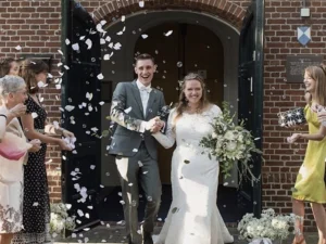 Een bruid en een bruidegom door de deur na de ceremonie met allemaal bloemblaadjes die in de lucht worden gegooid.