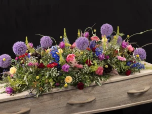 Sfeer kleuren, een rouw bloemstuk op een kist met bloemen in de kleuren paars, roze, geel, rood, blauw en groen, gemaakt door Bloeibloemen.nl