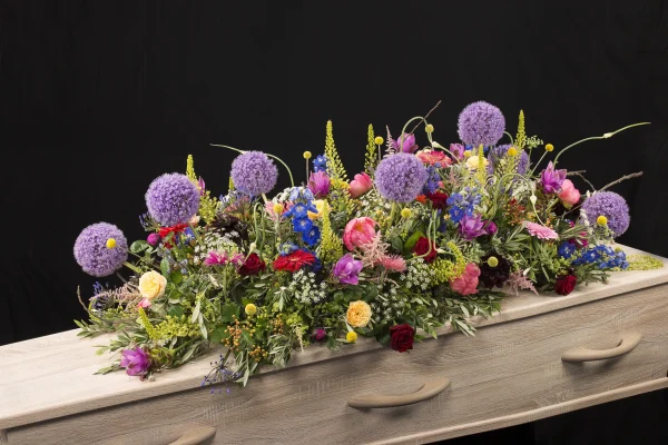 Sfeer kleuren, een rouw bloemstuk op een kist met bloemen in de kleuren paars, roze, geel, rood, blauw en groen, gemaakt door Bloeibloemen.nl