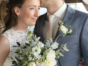 De bruidegom die de bruid een kus geeft op haar hoofd, de bruid heeft haar bruidsboeket vast.