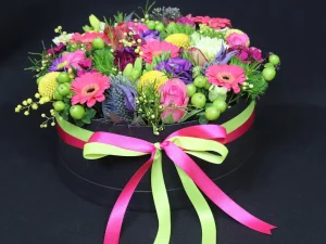 Flowerbox Color big, een box met verschillende soorten bloemen in de kleuren geel, roze, paars, rood en groen, gestoken in een blok oase. Deze bloemen zitten in een zwarte box met roze en groen lint eromheen.