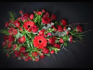 Rouw bloemstuk Drip of red, een rouwstuk in de vorm van een druppel met verschillende rode bloemen, afgewerkt met groen. Gemaakt door Bloeibloemen.nl