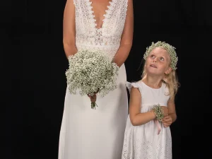 Een bruid en een bruidsmeisje, de bruid heeft een bruidsboeket in haar hand met witte bloemen en het bruidsmeisje heeft een haarkrans en bloemenarmband om, gemaakt door Bloeibloemen.nl