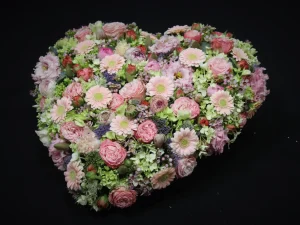 Rouw bloemstuk Hart of pastel. Een bloemstuk in de vorm van een hart, met roze, witte en paarse bloemen. Gemaakt door Bloeibloemen.nl