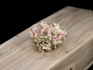 Rouw bloemstuk Love of the heart. Een bloemstuk in de vorm van een hart met roze en witte bloemen op een kist.