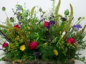 Een rouwstuk gestoken op een boomschors. Dit bloemstuk is gemaakt met verschillende kleuren bloemen zoals rood, geel en paars.