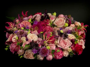 Een rouwkrans met bloemen voor een begrafenis in de kleuren roze, rood, paars en geel.