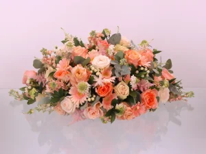 Bloemstuk Peach love gemaakt voor een begrafenis. Dit rouwstuk heeft verschillende oranje, zachtroze en witte bloemen.