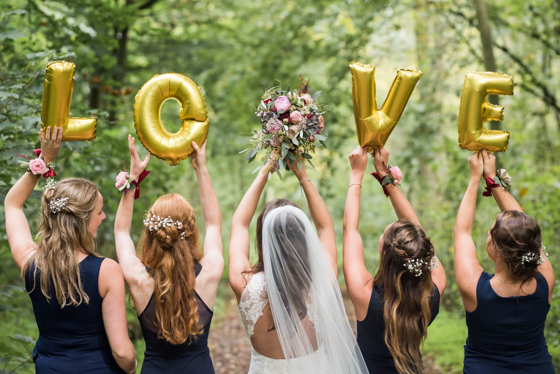 Vijf vrouwen op rij met ballonnen met Love en in het midden de bruid met een bruidsboeket met verschillende bloemen