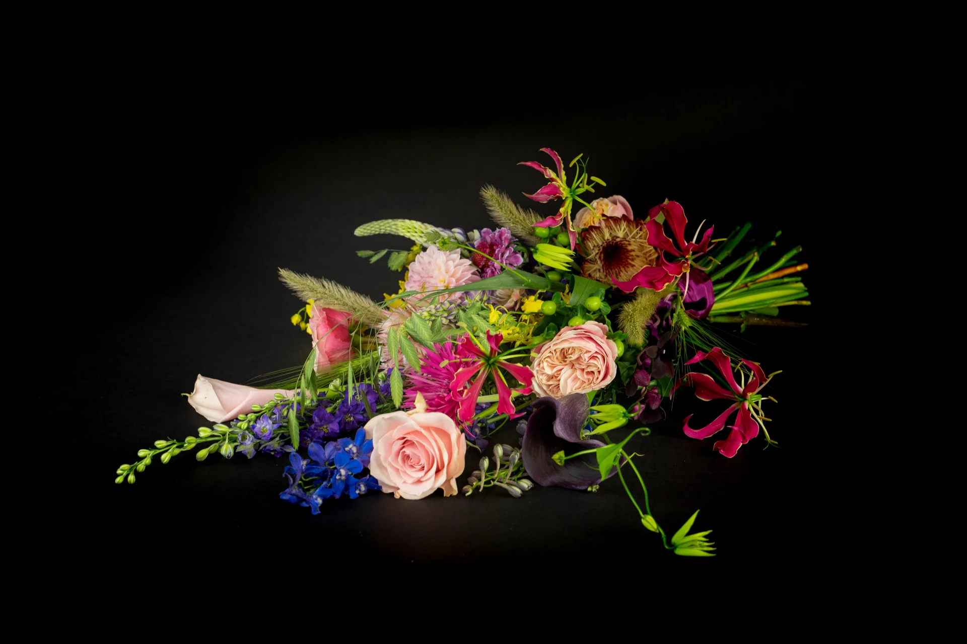 Een rouw bloemstuk met verschillende soorten en kleuren bloemen zoals rood, paars, lichtroze, blauw en geel.