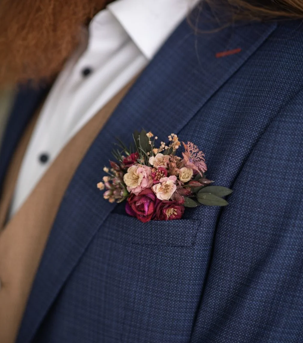 De corsage in het zakje van het pak. De corsage heeft zachtroze en rode kleuren.